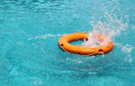 Orange life buoy splash water in the clear blue water swimming pool, for the emergence caseの写真素材