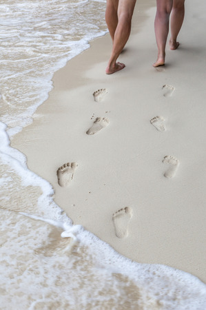 The sweet couple holding hands walking on the beach and their footprints in the sand around seashore.の写真素材