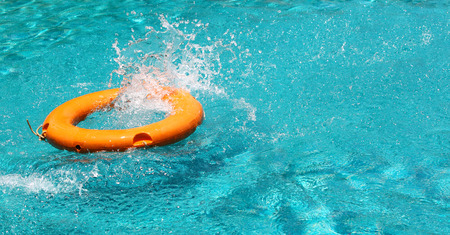Orange life buoy splash water in the clear blue water swimming pool, for the emergence case, use as the wallpaper, left space for the textの写真素材