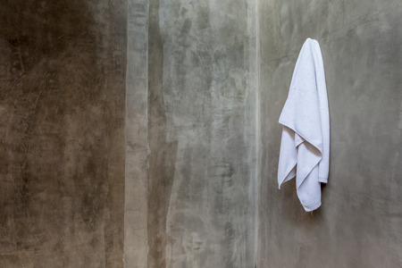Hanging white and clean towel draped on exposed concrete wall in the bathroom.の写真素材