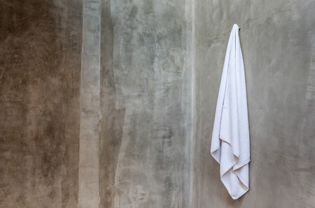 Clean and white towel is hanging on a hanger with concrete wall in the bathroom.の写真素材