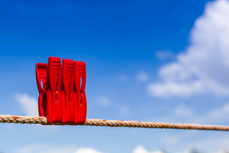 Three red plastic clothespins hang on a laundry line outside with the bright blue sky.の写真素材