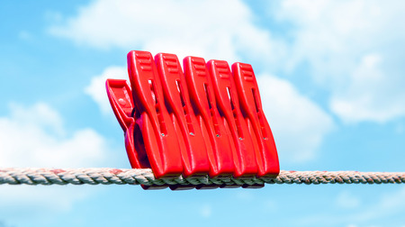 Five red plastic clothespins hang on the clothesline with blurry blue sky background.の写真素材