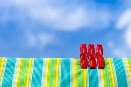 Three red plastic clothespins and multicolor cotton on clothesline with the blurry blue sky background.の写真素材