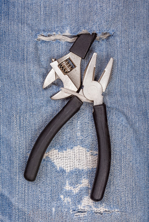 2 types of pliers black handle tool with torn blue jeans pattern background, concept for fixing and useful maintenance.の写真素材