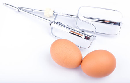 Two fresh eggs with set of auto beater whisks on white background.