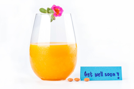 Fresh orange juice glass and pink flower on top, pills next to get well soon note on white background.の写真素材