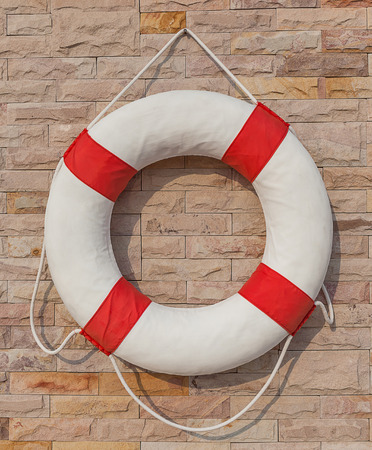 The white and red life buoy hanging on the brick wall around the swimming pool, for safety and rescue.の写真素材