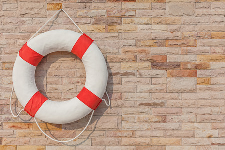 The life buoy is hanged on brick wall background nearby the swimming pool, for safety and rescue.の写真素材