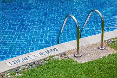 The metallic ladder and depth indicating sign with clear blue swimming pool.
