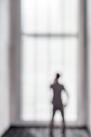 Blurred picture of business man using phone near the window in office building.の写真素材