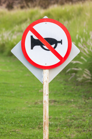 Silence zone in rural scene, the white and red circle warning sign of do not use vehicle horn with blurred background of flowering grass in agriculture farmland.の写真素材