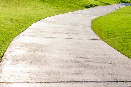 The single lane and curved cement pathway through in green golf course.の写真素材