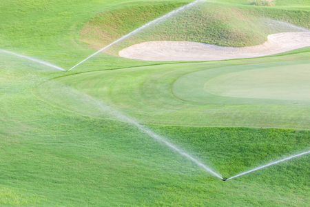 Two sprinklers watering system working in fairway and sand bunker of green golf course.の写真素材
