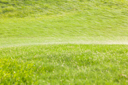 Closeup and soft focus watering drops from sprinkler spread over the green golf course in the morning time.の写真素材