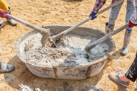 Concrete workers mixing the cement and sand in grunge steel salver, building construction site.の写真素材