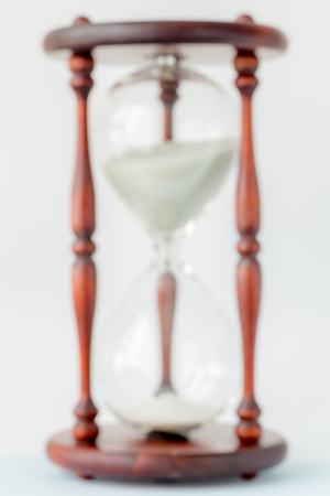 Blurred photo of vintage style of white sand crystal and wooden hourglass on white background, time...