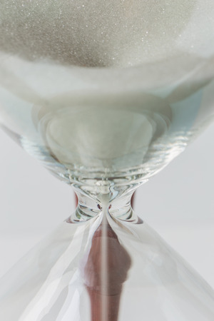 Close up white sand flowing of vintage wooden hourglass on white background, time concept.