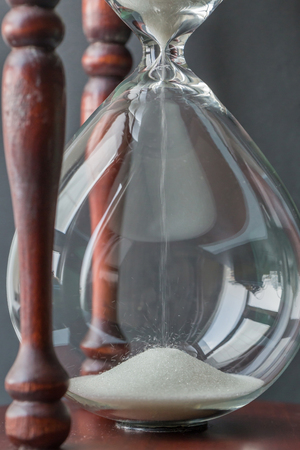 Fallen white sand crystal in vintage wooden hourglass with blurred background, time concept.