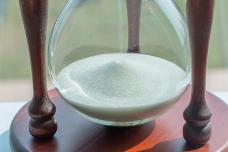 Flowing white sand crystal in vintage wooden hourglass with blurred background, time concept.の写真素材