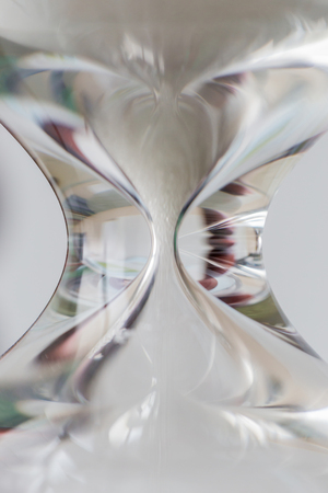 Close up white sand flowing motion of vintage wooden hourglass on white background, time concept.