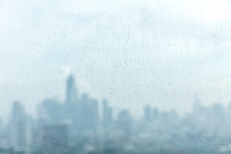 Rain drops on window glass and blurred cityscape and sunlight in background.の写真素材