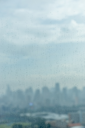 Rain drops on window glass and blurred cityscape and sunlight in background.の写真素材