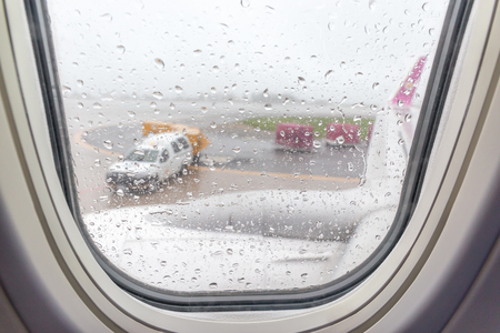 Blurred photo of rain drops from airplane window and airport runway in background.の写真素材