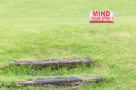 Mind your step warning sign to alert of natural wooden steps on green grass golf course.の写真素材