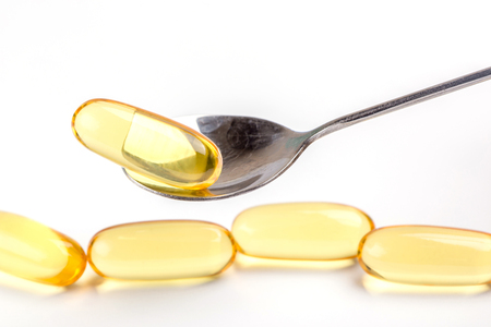 Close up a soft gel capsules on spoon with blurred another capsules in background, essential oil supplement intake concept.の写真素材