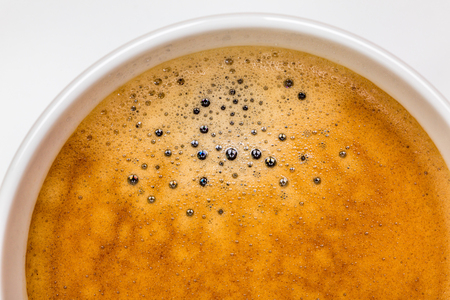 Detail of hot black coffee with foam bubbles in white cup with white background, morning coffee concept.の写真素材