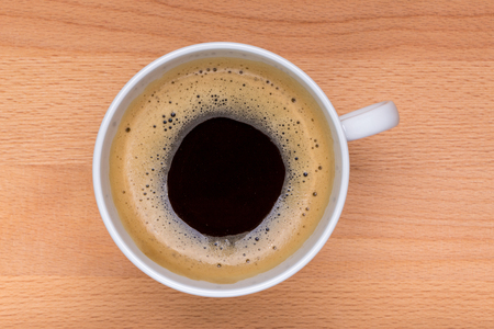 Detail of hot black coffee with some foaming on top in the white cup and wooden board in background, morning coffee concept.の写真素材