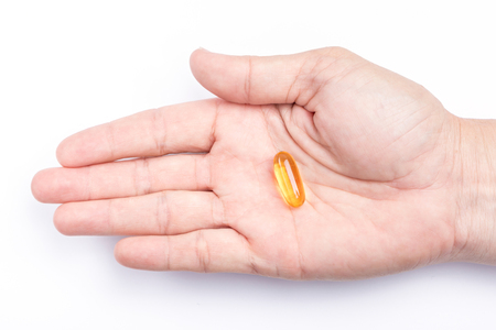 Close up yellow soft gel capsule in male hand with white background, concept of essential oil supplement intake.の写真素材