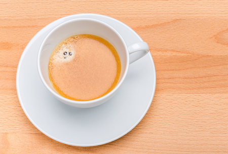 Hot black coffee with foam bubbles in white cup with wooden board in background, morning coffee concept.の写真素材
