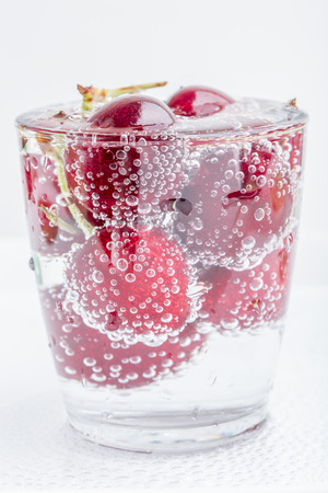 Group of sweet ripe cherries in a glass of sparkling soda water placed on white background, healthy drinking concept.の写真素材