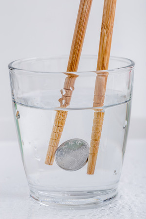 Japanese coin (yen) holding by wooden chopsticks in a glass of water isolated on white background, currency exchange concept.の写真素材