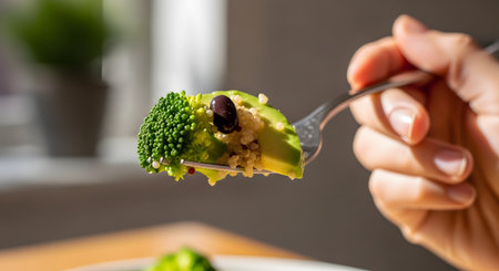 A close-up shot of a fork holding a perfect, healthy bite of a vegan meal. The forkful includes a fresh broccoli floret, creamy avocado, quinoa, and a black bean, showcasing a delicious and nutritious plant-based diet.の素材
