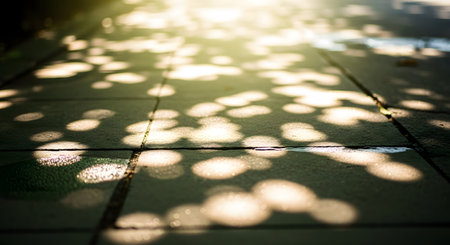 An atmospheric and dreamy photograph of dappled sunlight creating soft, out-of-focus spots of golden light on a paved path. This beautiful, abstract image of light and shadow evokes a warm, peaceful, and nostalgic feeling.の素材