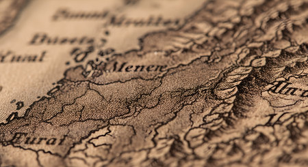 A macro photograph of a vintage, sepia-toned map with a very shallow depth of field. The focus is on the fine details of the textured paper and the intricate lines representing topography, evoking a sense of history, cartography, and adventure.の素材