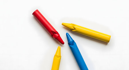 Four wax crayons in primary colorsâred, yellow, and blueâare arranged on a clean white background. This minimalist, top-down view represents simplicity, childhood creativity, art, and basic education.の素材