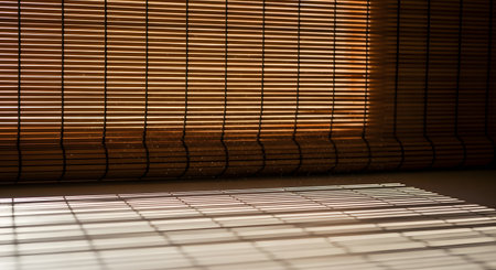 Warm, golden sunlight filters through horizontal bamboo blinds, casting a beautiful pattern of light and shadow onto a surface below. Dust motes dance in the sunbeams, creating a tranquil, warm, and atmospheric scene that evokes a sense of peace and quiet.の素材