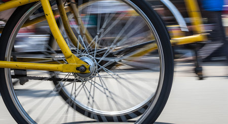 A dynamic panning photograph captures the close-up motion of a spinning yellow bicycle wheel. The blurred background effectively conveys a sense of high speed and movement, typical of urban transportation or a rickshaw ride.の素材