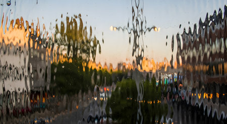 An abstract view of the outside world as seen through a pane of textured, wavy privacy glass. The scene of trees and buildings is distorted into a beautiful, impressionistic and painterly image of blurred colors and shapes, serving as a unique and artistic background.の素材