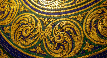 A close-up, detailed view of a traditional Thai mosaic pattern. The intricate design features swirling floral motifs in shimmering gold tiles, set against a background of deep blue and green tiles, showcasing exquisite craftsmanship and cultural art.の素材