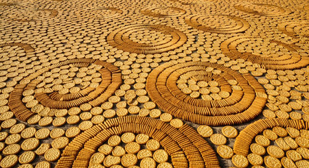 A vast art installation created from thousands of round biscuits arranged in large, swirling patterns of concentric circles. The overhead perspective highlights the impressive scale, texture, and repetitive design of the artwork, representing creativity and unconventional art.の素材