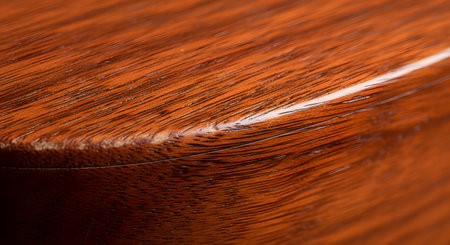 A detailed macro photograph captures the corner of a piece of polished wooden furniture. The rich, warm tones of the wood grain and the glossy varnish are clearly visible, highlighting the texture and craftsmanship. The image focuses on the smooth, curved edge and the fine lines of the wood.の素材