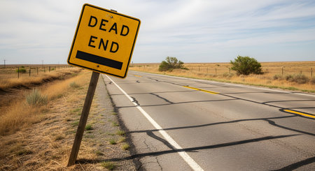 A crooked, yellow 'DEAD END' road sign stands on the side of a cracked asphalt road that stretches into a vast, empty, and arid landscape. The image conveys concepts of finality, limitation, obstacles, being lost, or the end of a journey. The desolate scenery adds to the feeling of isolation.の素材