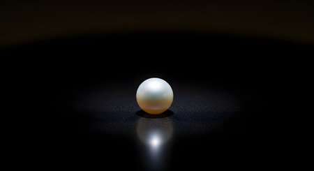 A single, luminous white pearl sits on a dark, reflective surface, creating a soft reflection below. The minimalist and elegant composition highlights the pearl's perfection, value, and beauty, symbolizing luxury and purity.の素材