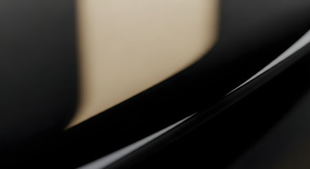 An elegant abstract macro photograph of a sleek, glossy black surface with a smooth curve and a soft gold or beige reflection. The minimalist composition creates a sophisticated and luxurious background for design or product placement.の素材
