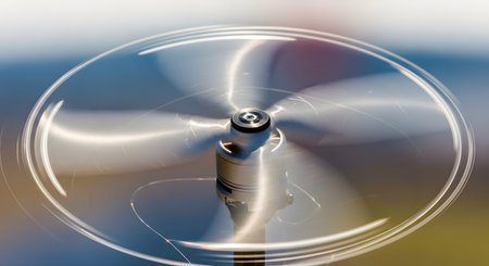 A long-exposure, close-up photograph of a small, metallic fan or propeller spinning rapidly. The motion blur creates circular light trails, while the central hub remains in sharp focus.の素材